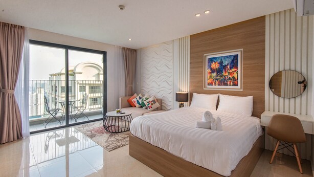A modern hotel room with a large bed, a desk, a chair, a round mirror, a painting, and a balcony with a city view.