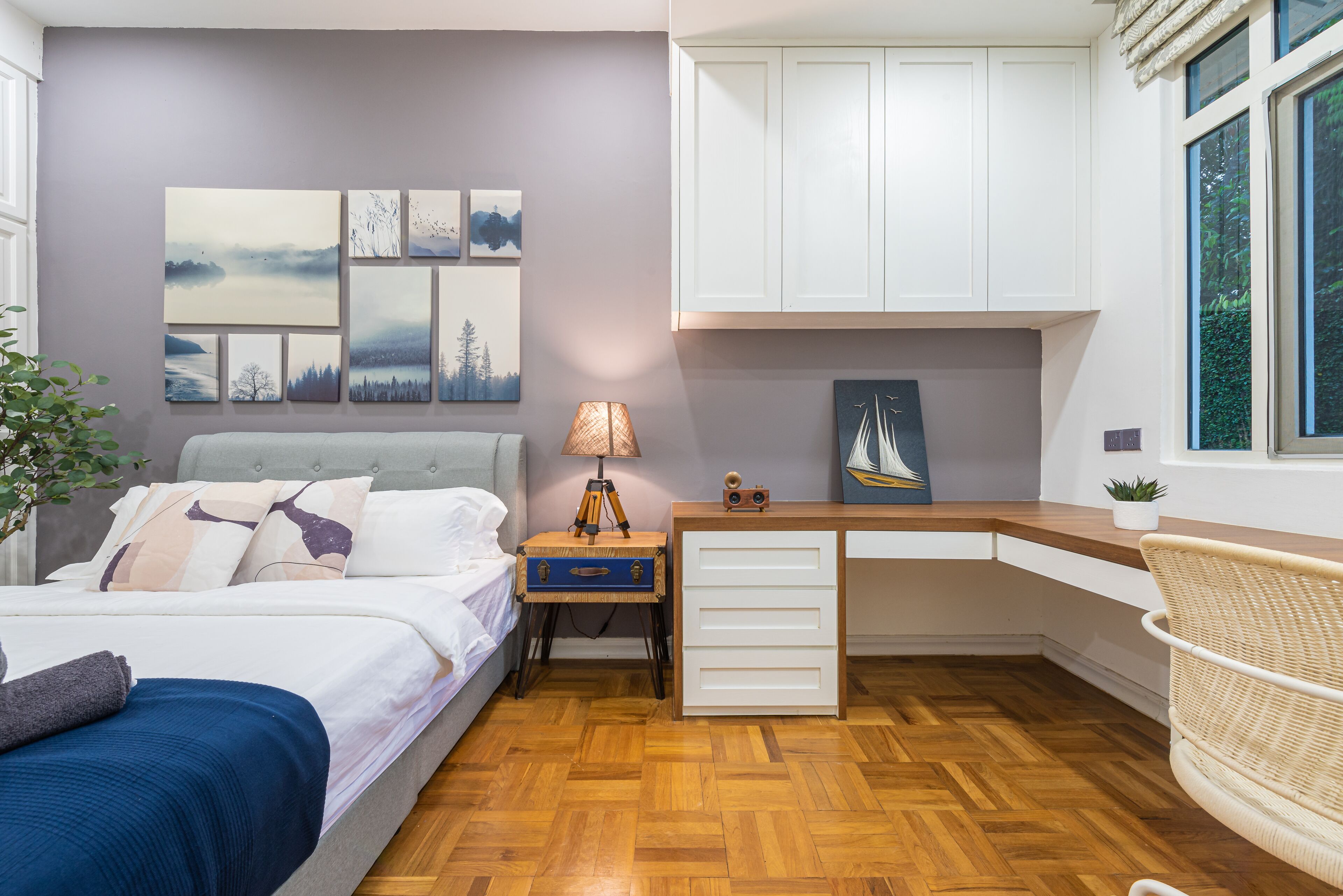 A bedroom with a bed, a desk, a lamp, and wall art.