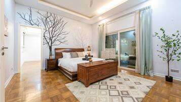 A bedroom with a wooden bed, a nightstand, a dresser, a large window with curtains, and a potted plant.