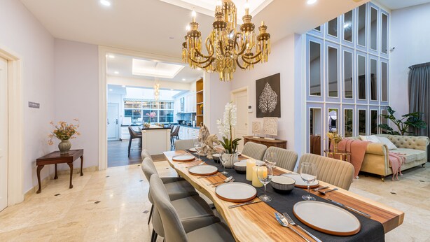 Un comedor amplio con una larga mesa de madera dispuesta para seis personas, rodeada de sillas modernas. Un gran candelabro cuelga del techo, y la habitación cuenta con un ventanal con vistas al exterior.