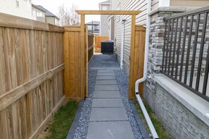 A narrow pathway with a wooden fence on one side and a stone wall on the other, leading to a gate.