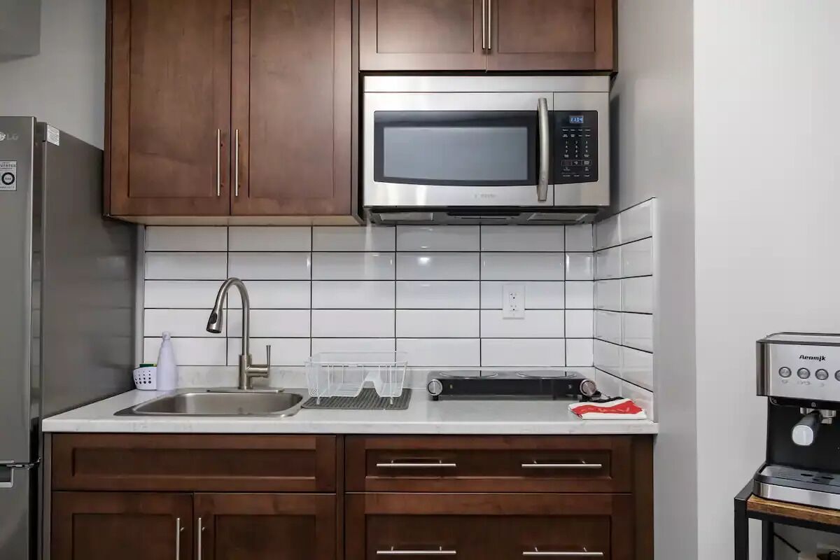 A kitchen with wooden cabinets, a stainless steel microwave, a sink, and a coffee machine.