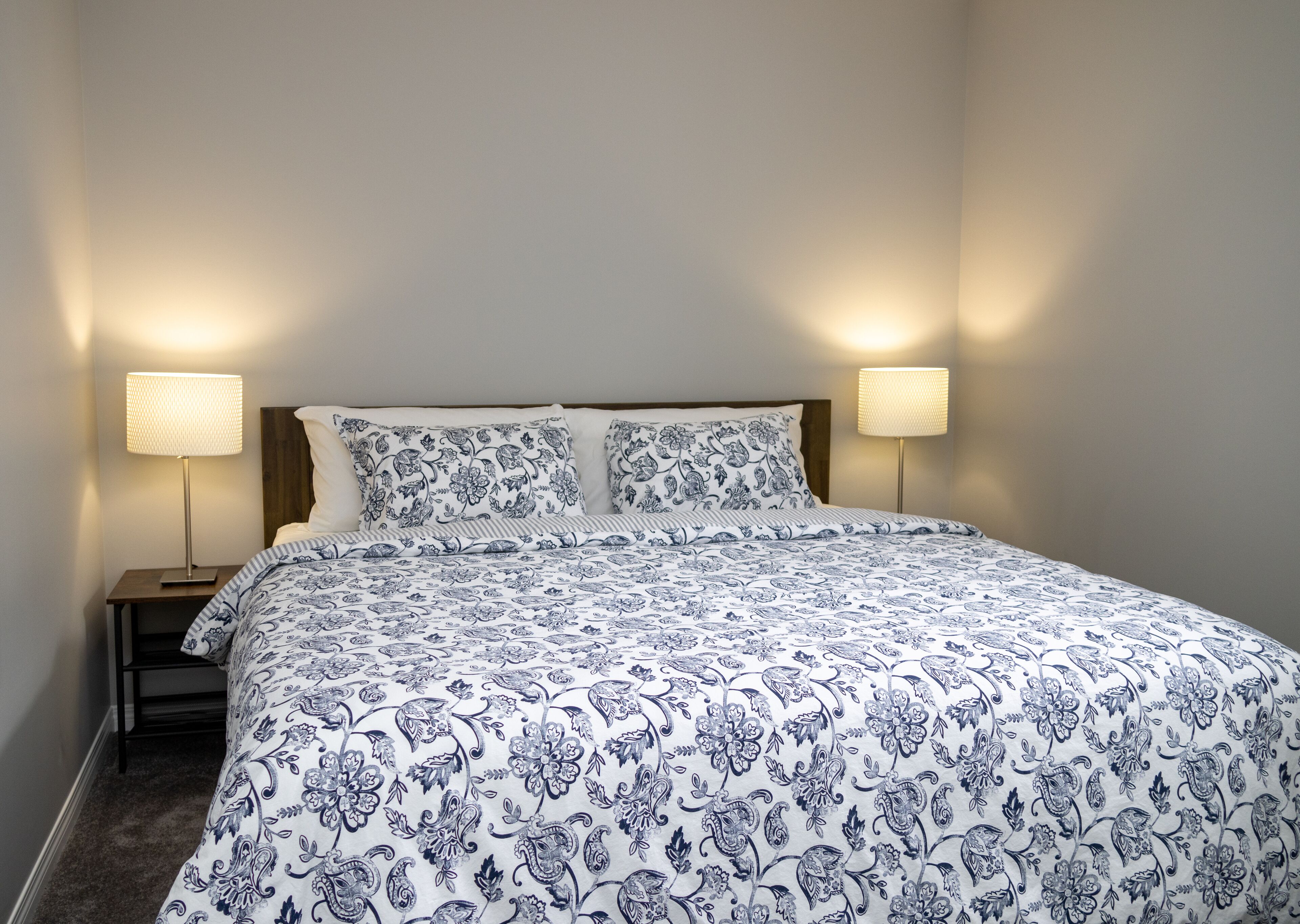 Una cama bien hecha con un edredón estampado, dos lámparas de noche y un cabecero de madera.