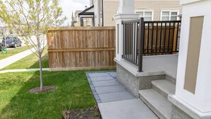 Ein Wohnhaus mit Holzzaun, einem kleinen Baum und einem Betonweg, der zu einer weißen Treppe führt.