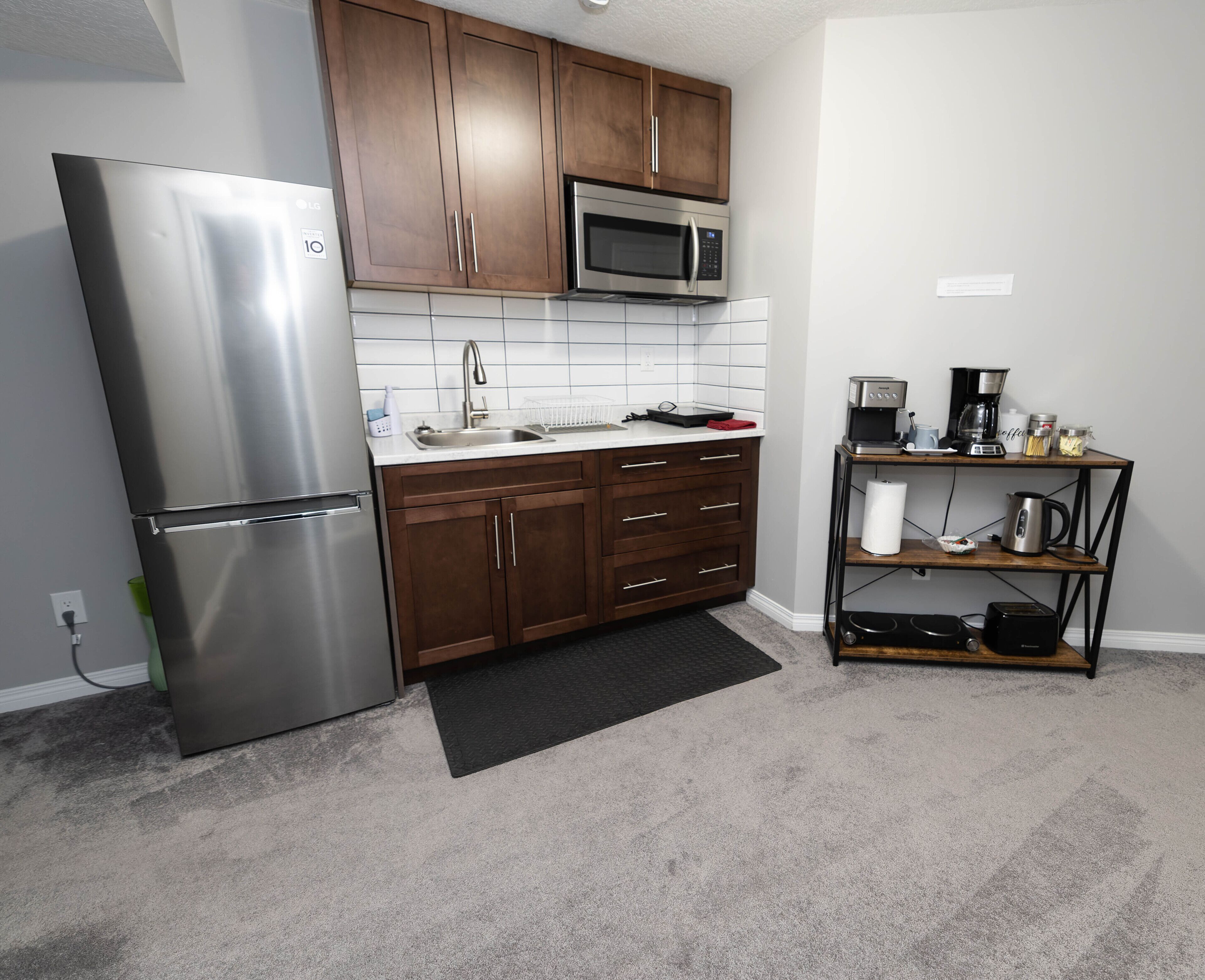 Cocina compacta con refrigerador de acero inoxidable, microondas y cafetera sobre una repisa de madera.