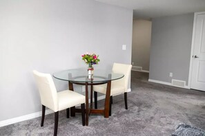 A dining area with a glass table and four chairs, a vase with flowers, and a carpeted floor.
