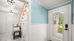 Un couloir avec une porte blanche, un banc et un escalier avec des marches en bois.