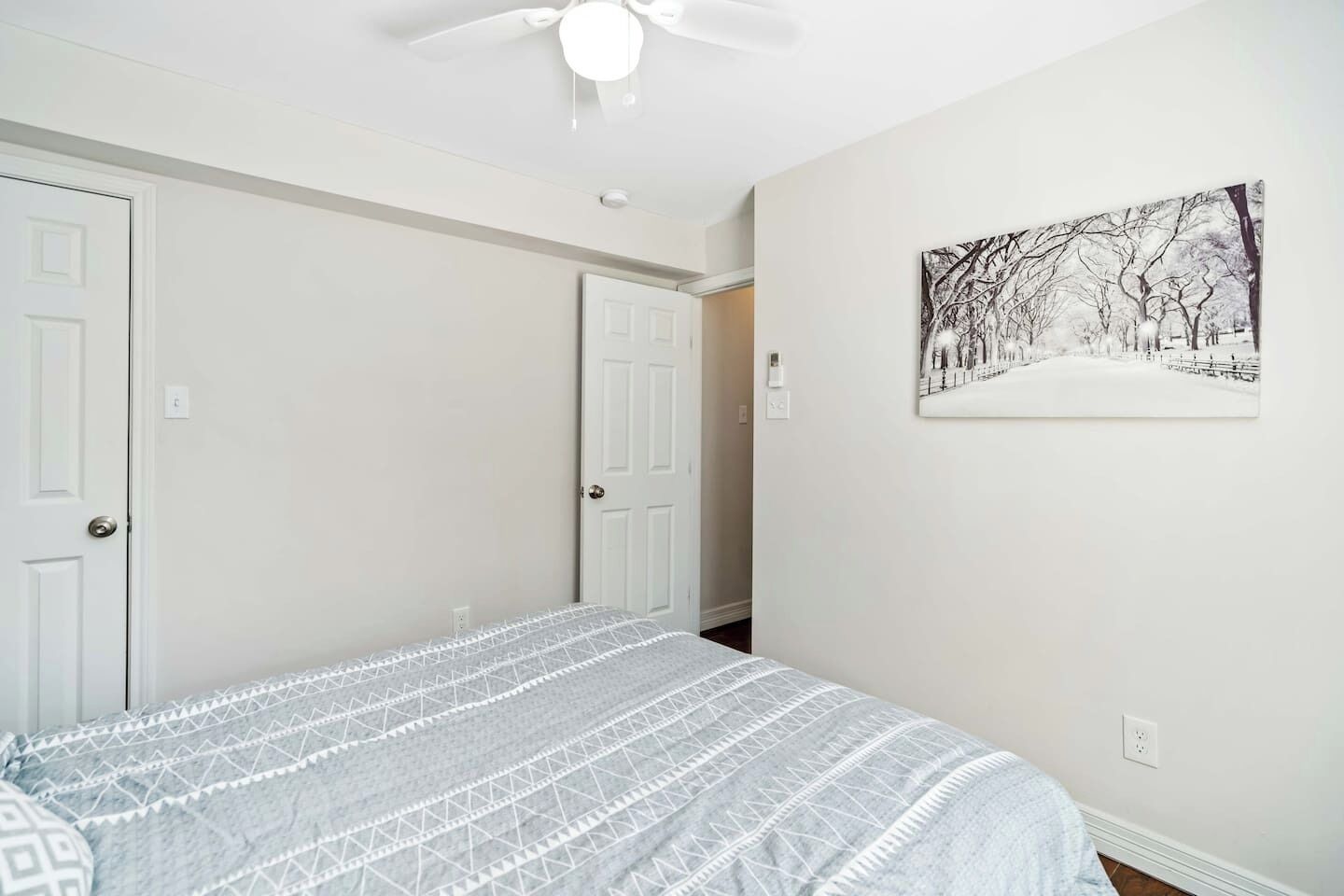 A bedroom with a bed, two white doors, a ceiling fan, and a wall-mounted picture.