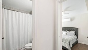 A bathroom with a shower curtain and toilet, and a bedroom with a bed and nightstand. - Texas Med Center Stunning & Vibrant Stay (Houston)