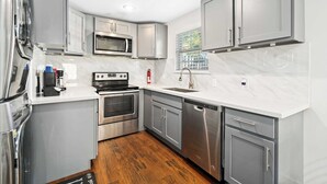 A modern kitchen with stainless steel appliances, grey cabinetry, and a white marble countertop. - Texas Med Center Stunning & Vibrant Stay (Houston)