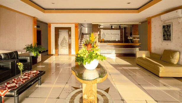 A hotel lobby with a reception desk, a sofa, a coffee table with a vase of flowers, and a patterned rug. - The Kanjeng Hotel Kuta (Kuta)