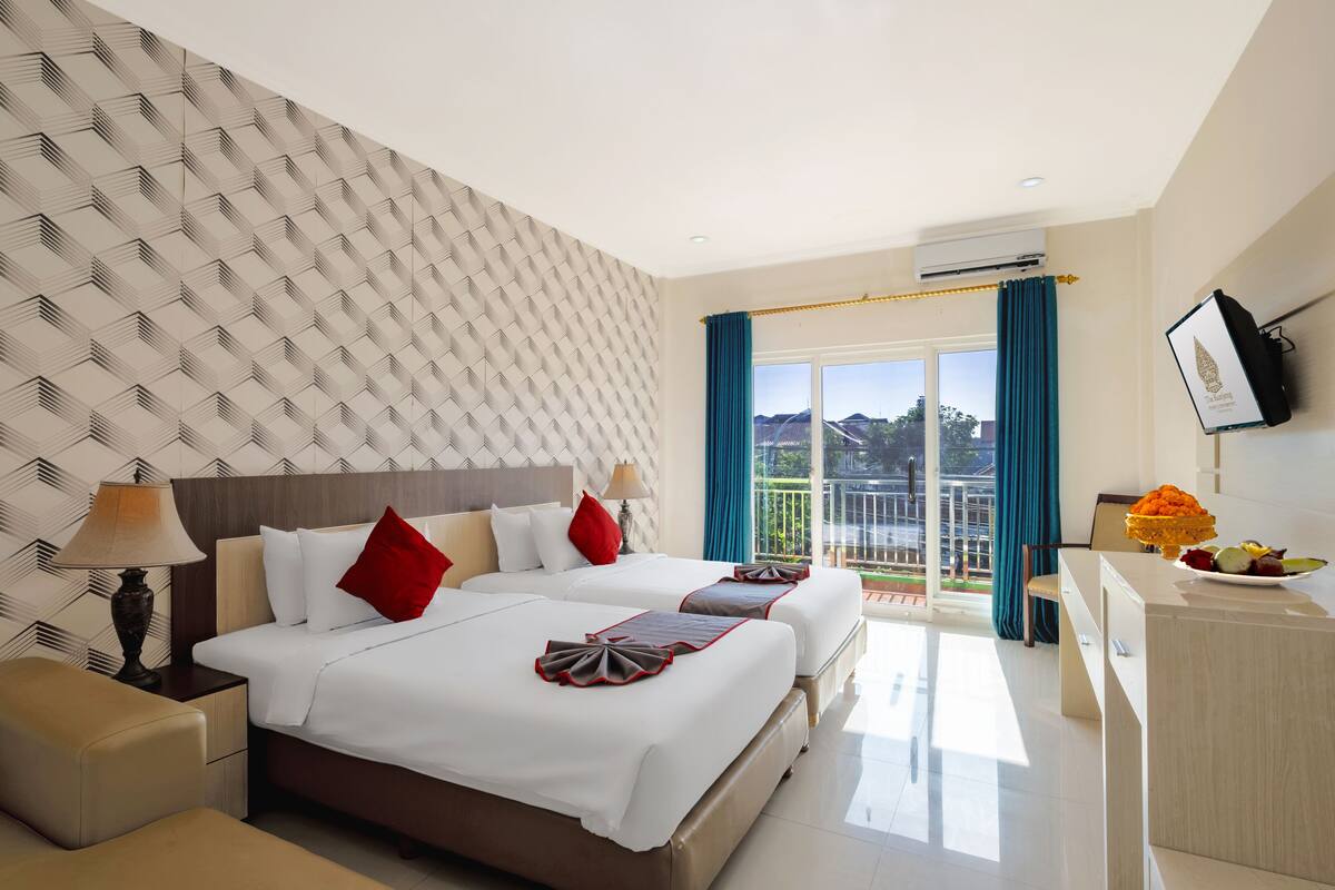 A hotel room with two beds, a TV, a desk, and a balcony with a view.