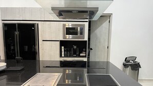 A modern kitchen with a black countertop, stainless steel appliances, and a trash can. - Casa en Riviera Maya con alberca privada (Puerto Morelos)