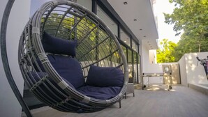 A hanging chair with cushions in an outdoor area with a modern building in the background. - Casa en Riviera Maya con alberca privada (Puerto Morelos)