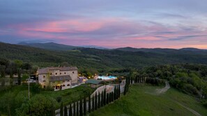 A stone building with a swimming pool, surrounded by lush greenery and hills. - Guado al Sole 26 4 Emma Villas (Pomarance)