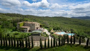 A large stone building with a swimming pool and outdoor seating area surrounded by lush greenery and mountains. - Guado al Sole 26 4 Emma Villas (Pomarance)