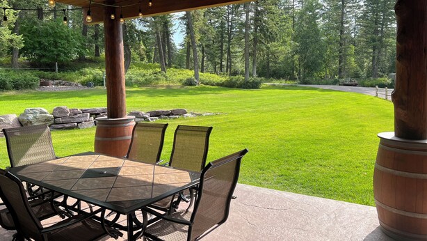Patio esterno con tavolo e sedie, circondato da una pergola in legno e luci a stringa.