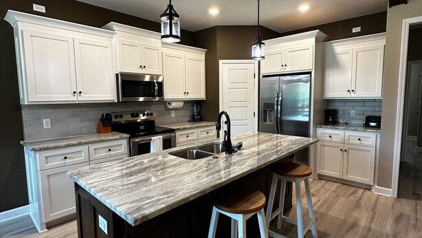 A modern kitchen with white cabinets, a large island with stools, stainless steel appliances, and pendant lighting. - Round Mountain Lazy Days (Conway)