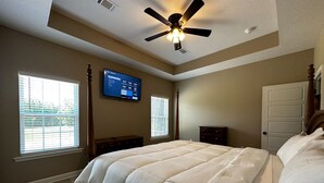 A bedroom with a bed, a ceiling fan, a TV mounted on the wall, and a window with blinds. - Round Mountain Lazy Days (Conway)