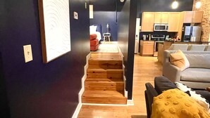 Un intérieur moderne avec un escalier menant à une chambre, un espace de vie avec un canapé et une cuisine dotée de meubles et d’appareils électroménagers en bois.