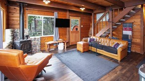 A cozy cabin interior with a stone fireplace, leather sofa, and a staircase leading to a loft.
