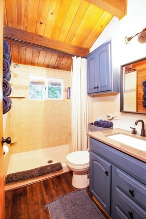 Un bagno con soffitto in legno, una vasca da bagno, un water, un lavandino con uno specchio e una finestra.