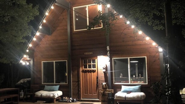 A two-story wooden cabin with a porch, large windows, and string lights.