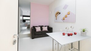 A modern room with a grey sofa, a white table, and a pink wall. There are apples and bananas on the table, and a plant in a pot. - WHITE HOUSES, Modern and functional studio apartment (bologna)