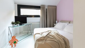 A modern hotel room with a glass desk, a bed with a beige blanket, a TV, and a window with curtains. - WHITE HOUSES, Modern and functional studio apartment (bologna)