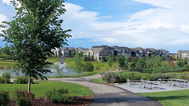 A paved pathway leading to a residential area with houses and a small body of water. - Amazing Basement Suite With a Dedicated Workspace (Airdrie)