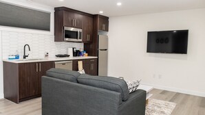 A modern kitchen with dark wooden cabinets, stainless steel appliances, and a white tiled backsplash. - Amazing Basement Suite With a Dedicated Workspace (Airdrie)