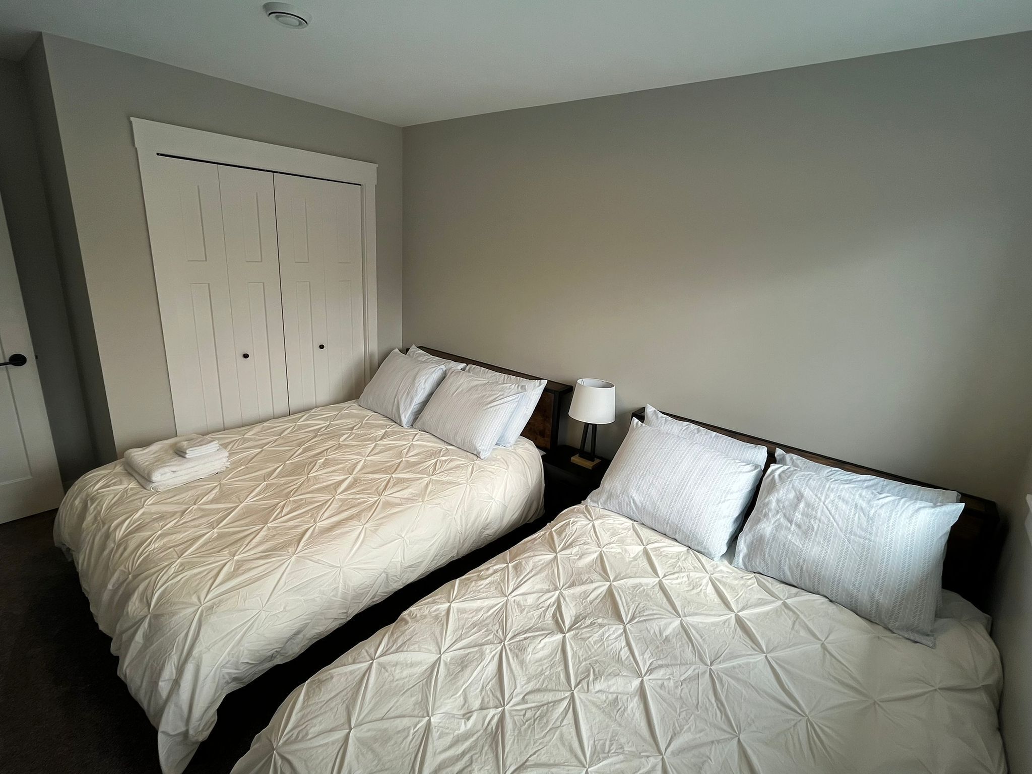 A hotel room with two beds, a wardrobe, and a nightstand with a lamp.