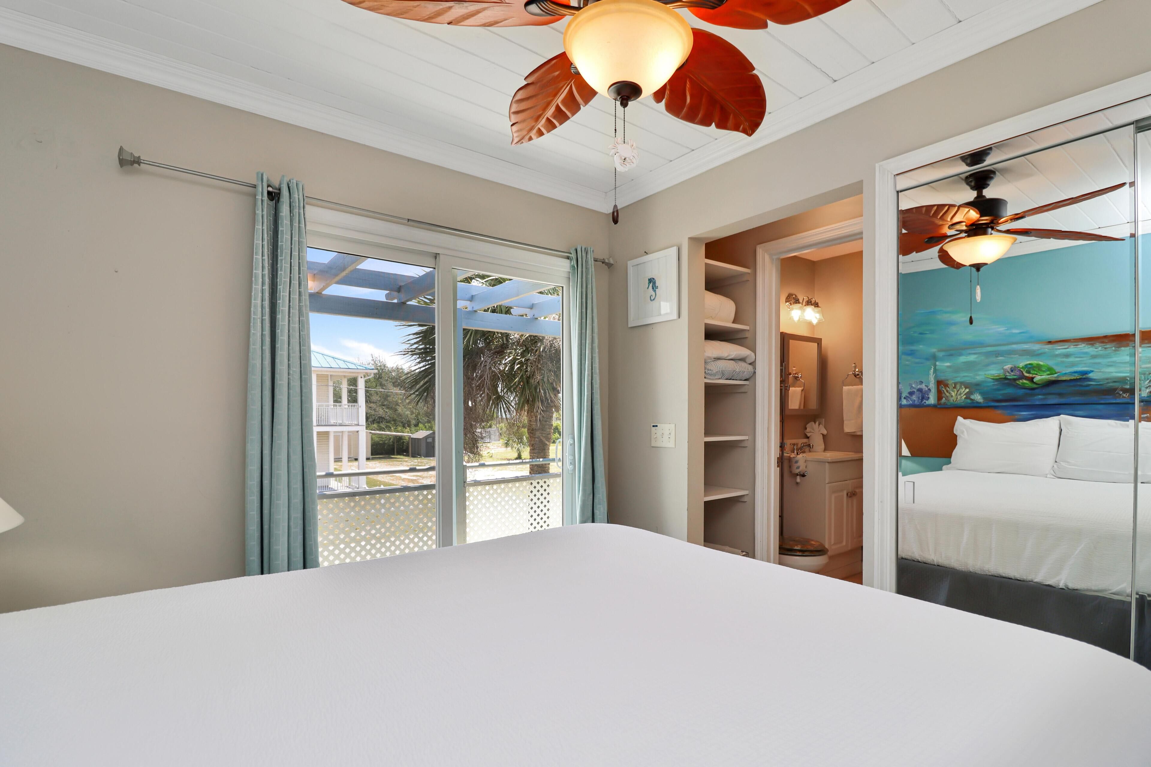 Een slaapkamer met een groot bed, een plafondventilator, uitzicht op het omliggende landschap door een schuifdeur, en een badkamer met douche en toilet.