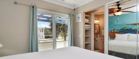 Een slaapkamer met een groot bed, een plafondventilator, uitzicht op het omliggende landschap door een schuifdeur, en een badkamer met douche en toilet.