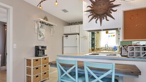 Une cuisine dotée d’un îlot central, de meubles blancs, d’une machine à café et d’une décoration sur le thème du soleil.
