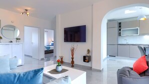 Uma sala de estar moderna com sofá, mesa de centro e área de cozinha com televisão e armários.