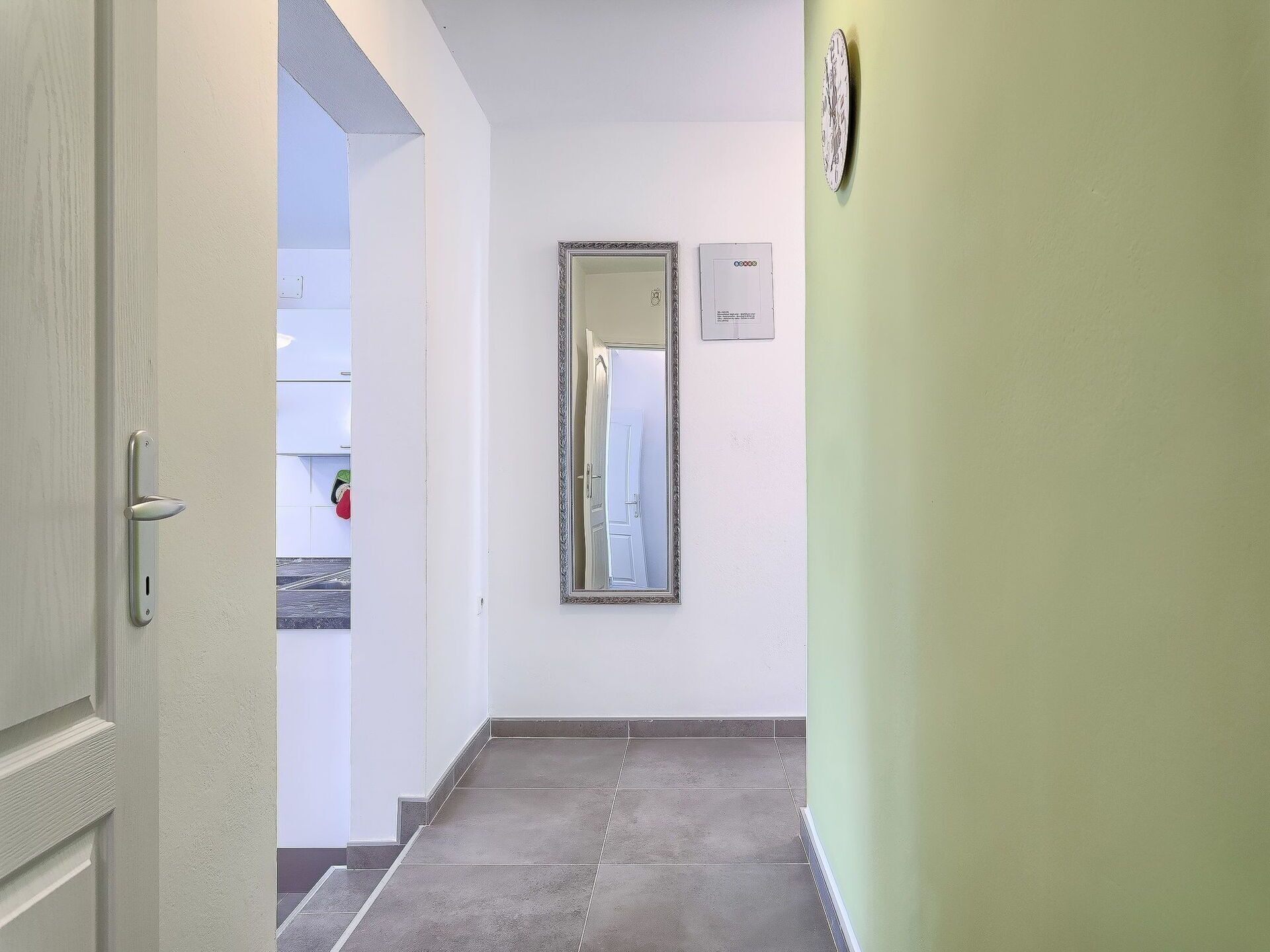 A hallway with a door, a mirror, and a light switch on the wall.