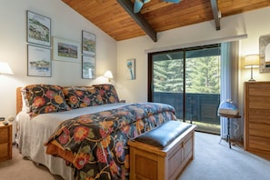 Quarto com cama grande, um banco, cômoda e porta de vidro corrediça para área externa.