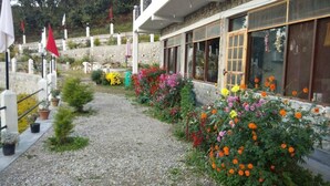 A building with a gravel pathway, potted plants, and a variety of flowers. - The Parijat Retreat (Bhikyasain)