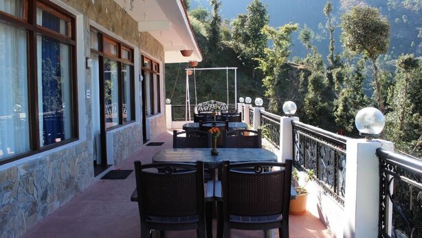 A balcony with a table and chairs, overlooking a mountainous landscape. - The Parijat Retreat (Bhikyasain)
