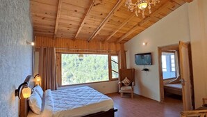 A bedroom with a bed, a chair, a TV, and a window with a view of trees. - The Parijat Retreat (Bhikyasain)