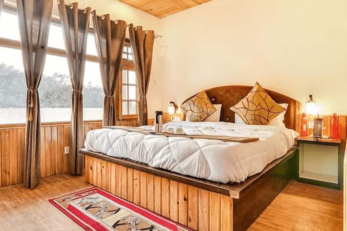 A wooden-framed bed with white bedding, a red and beige patterned rug, and a nightstand with a lamp.