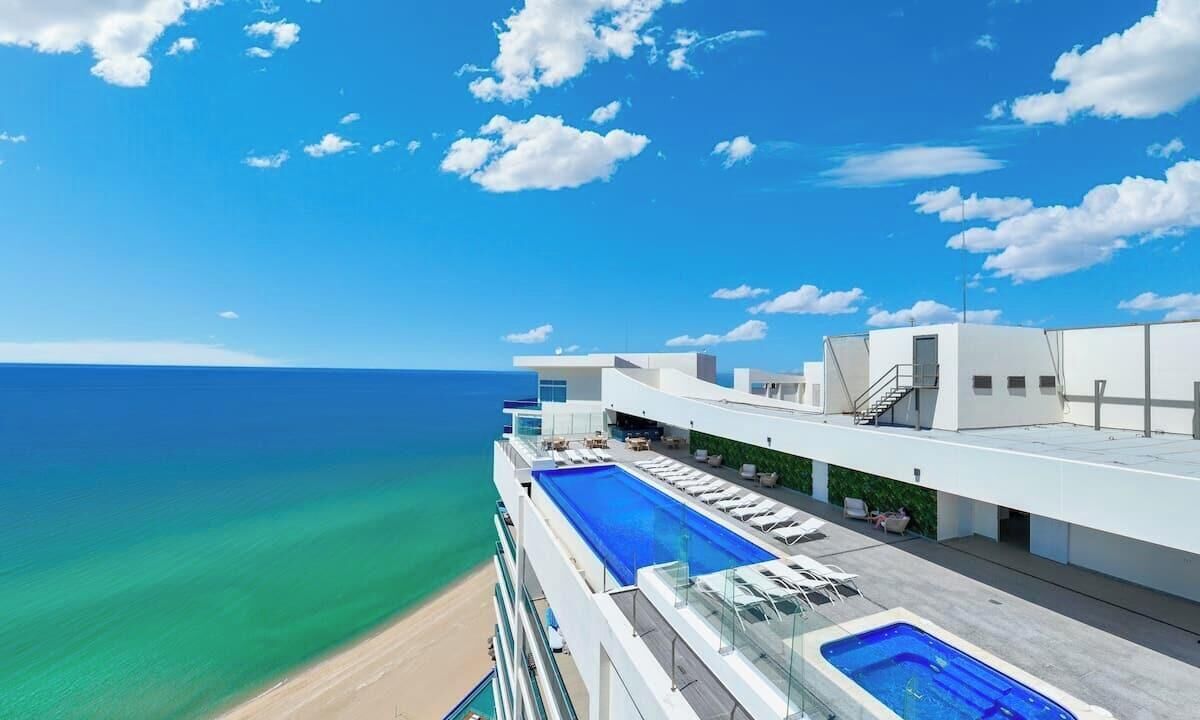 Un hôtel moderne doté d’une piscine sur le toit, offrant une vue sur une plage et l’océan.
