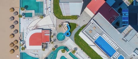 Vista aérea de un complejo turístico con varias piscinas, una zona de playa y un edificio de techo rojo.