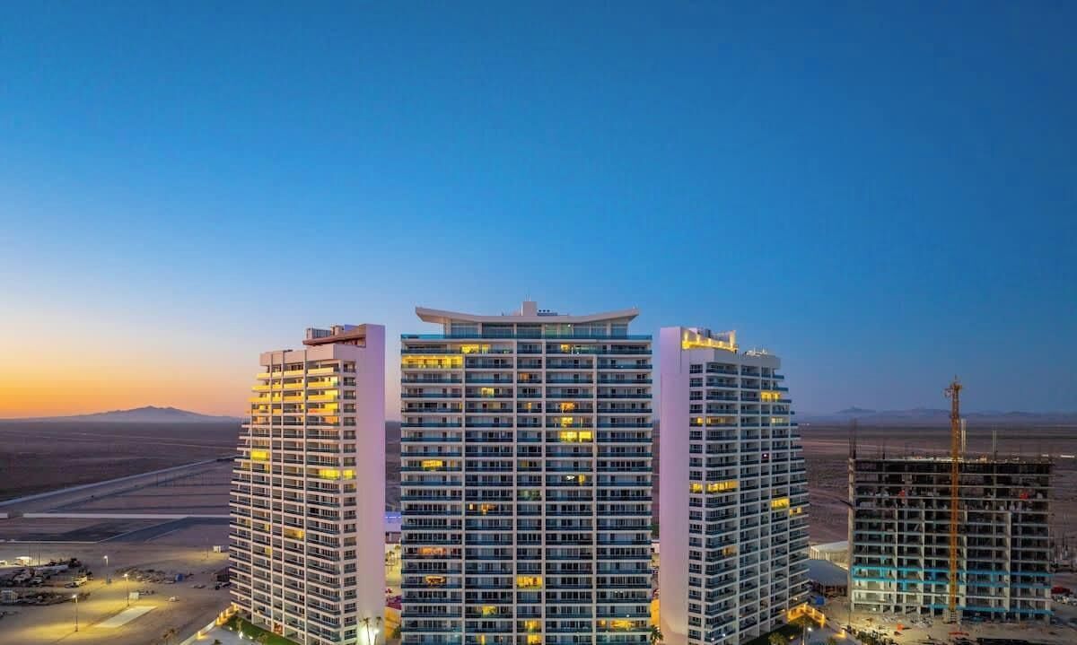 Een hoog hotel met meerdere verdiepingen, een zwembad en een woestijnlandschap op de achtergrond.