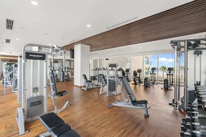 A gym with various exercise machines, benches, and a wooden floor.