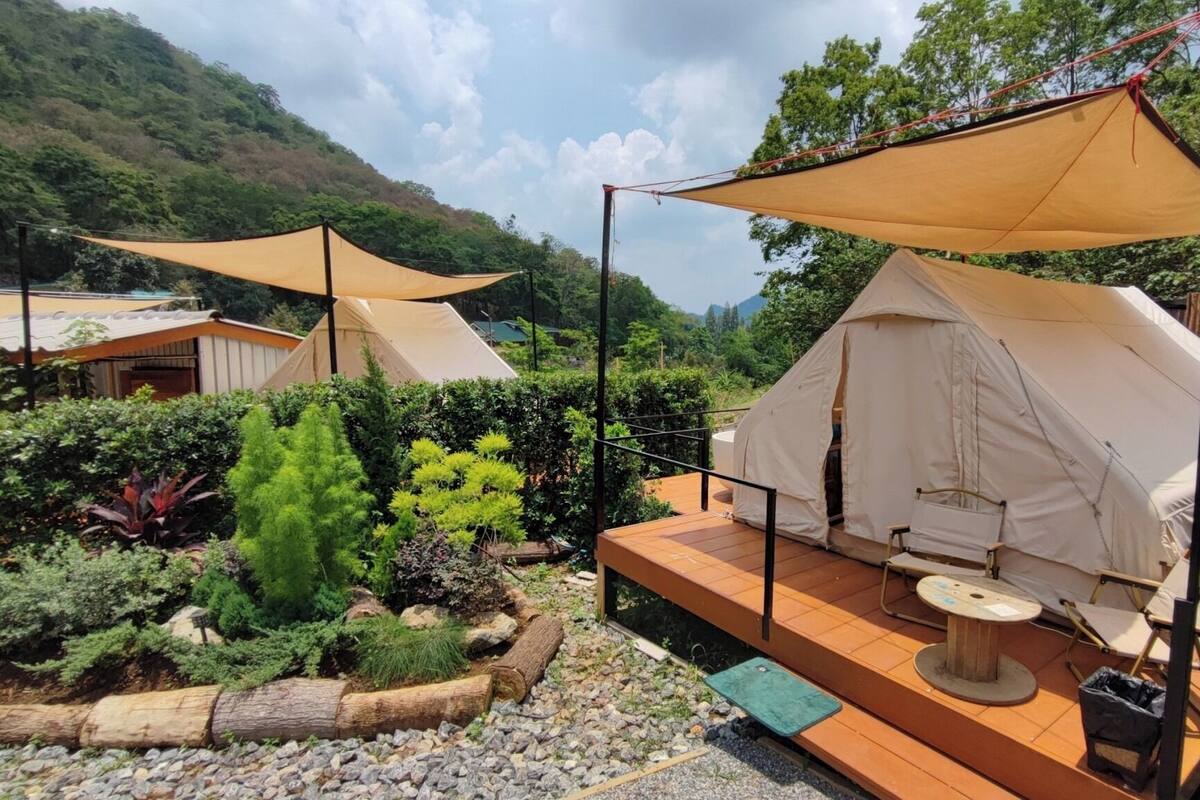 Un terrain de camping avec deux tentes, dont une dotée d’une terrasse en bois et de sièges, le tout entouré de verdure et avec une chaîne de montagnes en arrière-plan.