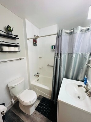 Een badkamer met een toilet, een douche met gordijn, een wastafel en planken met handdoeken.
