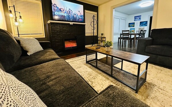 A living room with a fireplace, a television, and a dining area visible through an open door.