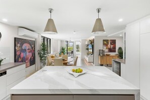 Uma cozinha moderna com ilha de mármore, iluminação pendente e um espaço de refeições com mesa e cadeiras.